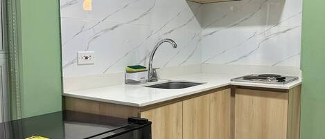Cocina compacta con refrigerador negro, un lavamanos y armarios de madera.