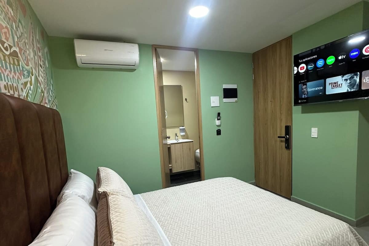 Une chambre d’hôtel équipée d’un lit, d’une tête de lit en bois, d’un téléviseur à écran plat fixé au mur et d’un appareil de climatisation également fixé au mur.