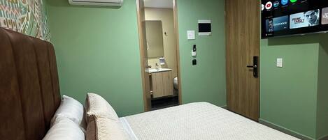 A hotel room with a bed, a wooden headboard, a flat-screen TV mounted on the wall, and an air conditioning unit on the wall.
