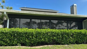 A modern building with a large glass window wall, a well-maintained hedge, and a clear blue sky. - Immaculate 3 bedroom villa: updated amenities on the Prestigious IMG Golf Course (Bradenton)