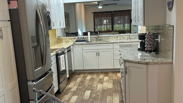 A modern kitchen with stainless steel appliances, wooden flooring, and white cabinetry. - Immaculate 3 bedroom villa: updated amenities on the Prestigious IMG Golf Course (Bradenton)