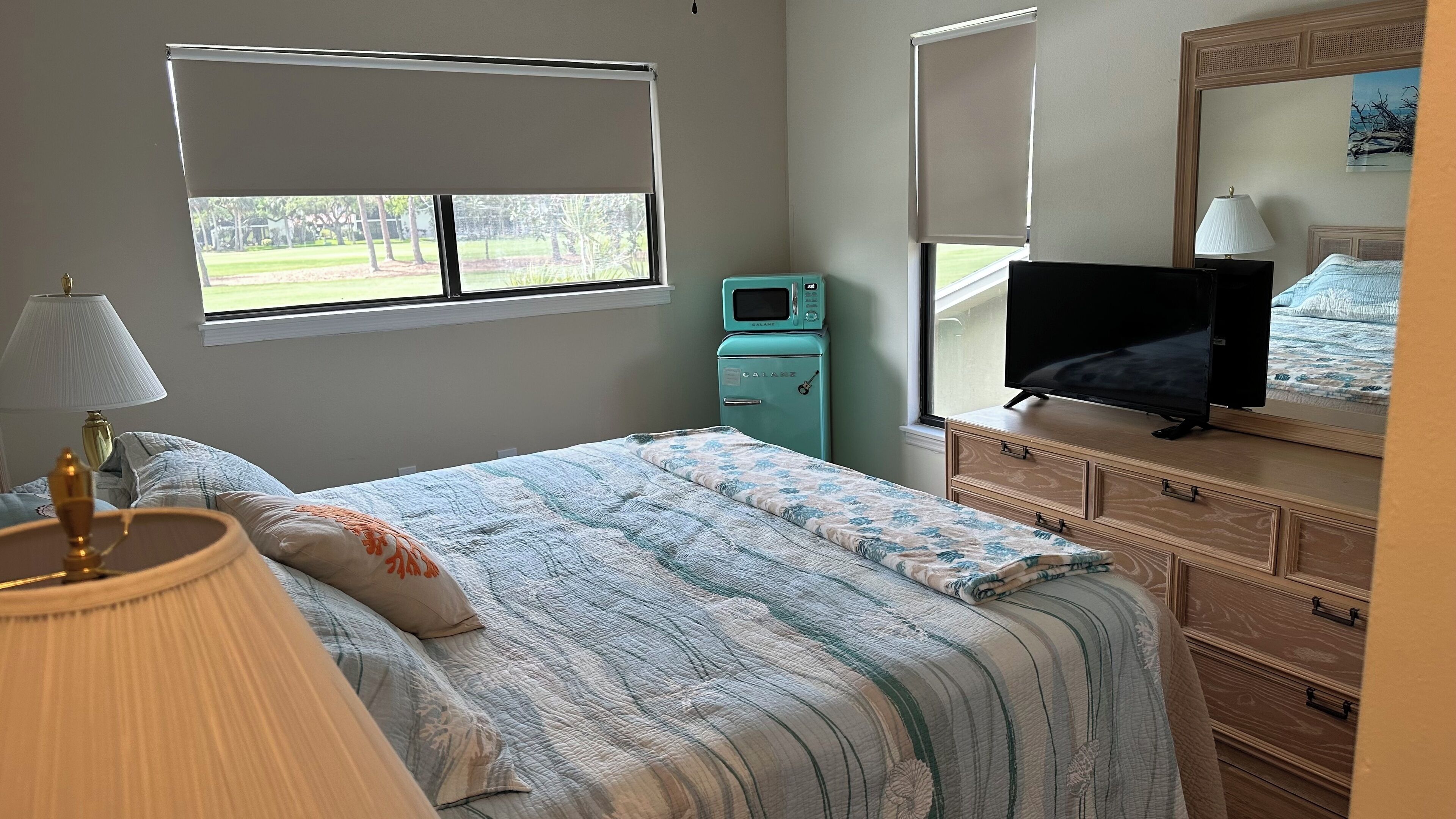 Ein Schlafzimmer mit Bett, Fernseher, Mikrowelle, Lampe und einem Schminktisch.