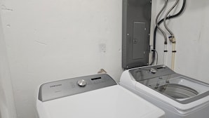 Un lave-linge et un sèche-linge à chargement frontal, installés dans une buanderie, avec un panneau de commande situé au-dessus du sèche-linge.