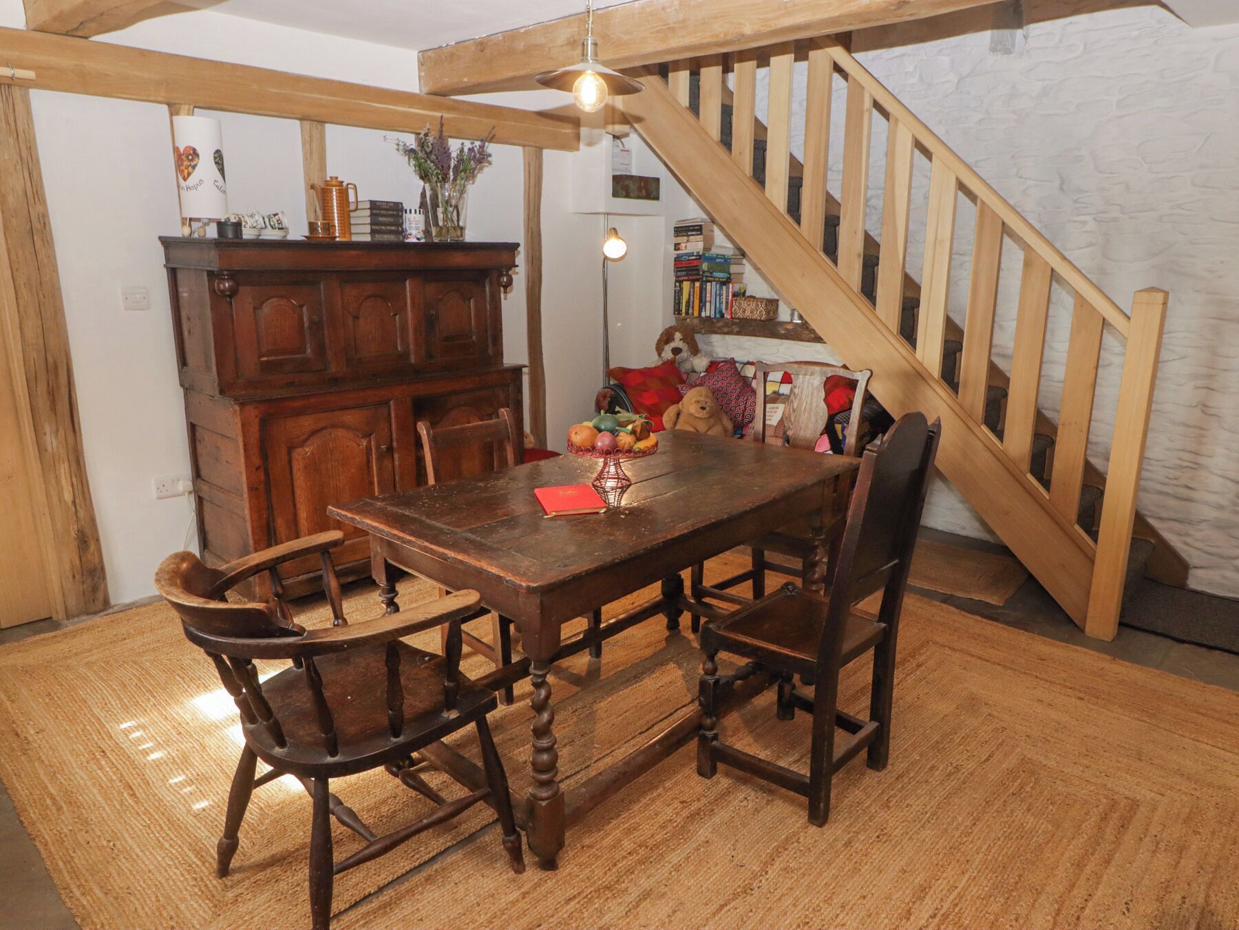 A wooden dining table with chairs, a wooden staircase, and a bookshelf with books and decorative items.