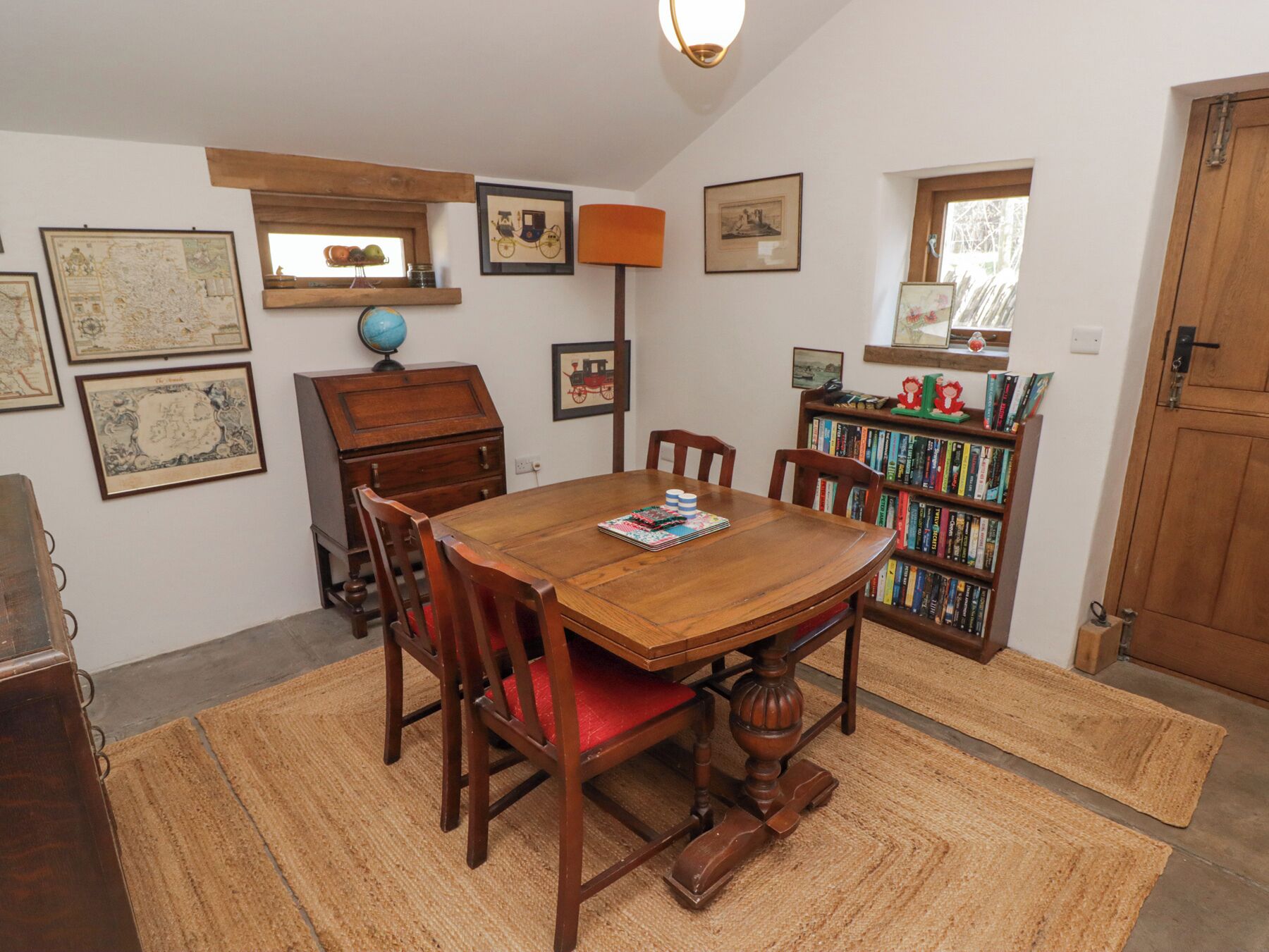 A dining room with a wooden table and chairs, a bookshelf, and various framed pictures on the walls.