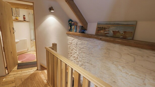 Una scala in legno con parete in pietra, ringhiera in legno e un quadro appeso al muro.