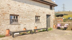 Un edificio in pietra con una panchina, due piante in vaso e una sedia.