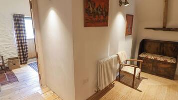A cozy room with a wooden floor, a radiator, a bench with a floral cushion, and two wall-mounted lamps.