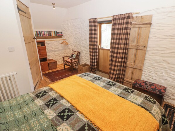 Une chambre à coucher avec un lit, une chaise, une petite table, une bibliothèque et une fenêtre avec des rideaux.