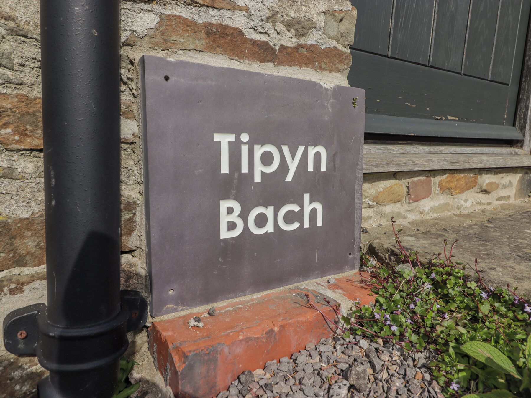 A sign with the text "Tipyn Bach" mounted on a brick wall.
