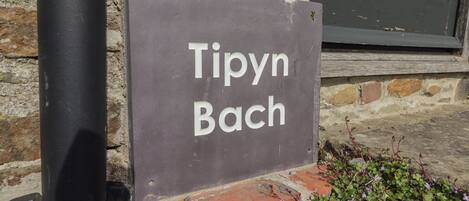 A sign with the text "Tipyn Bach" mounted on a brick wall.