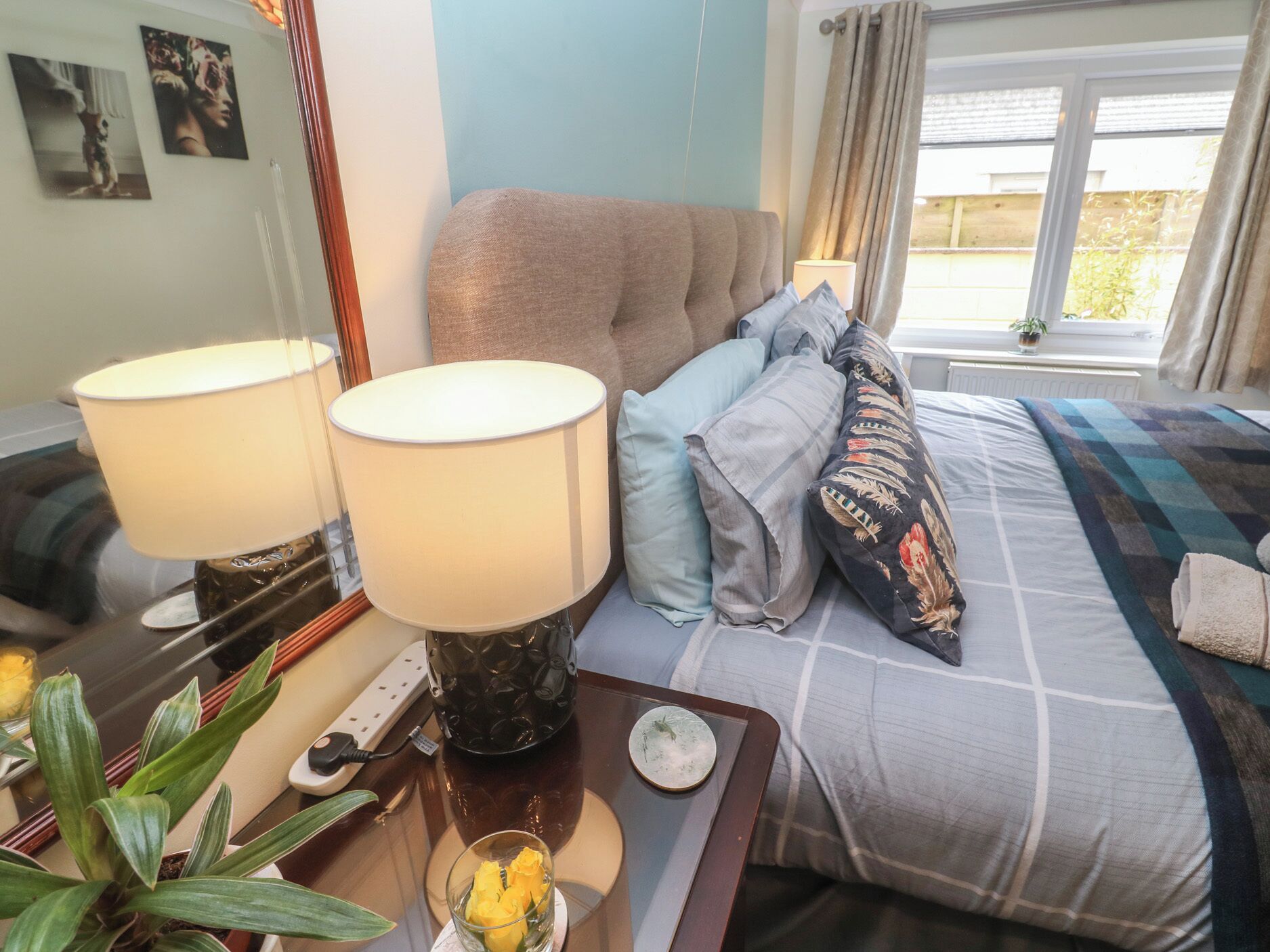 Un dormitorio con una cama, dos lámparas de noche, una mesita de noche con una planta y una ventana con cortinas.