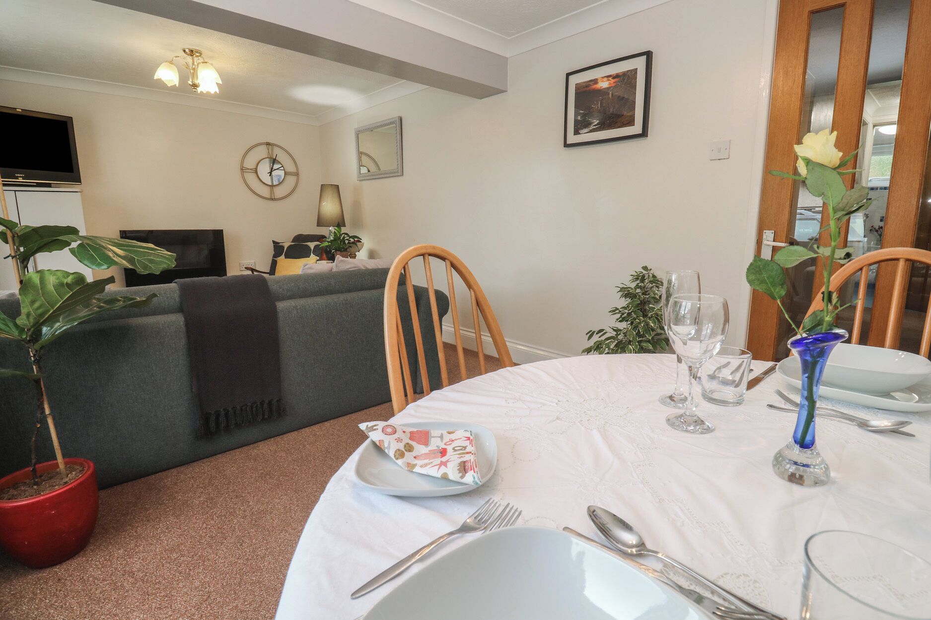A dining area with a round table set for two, a television in the background, and a sofa with a blanket.