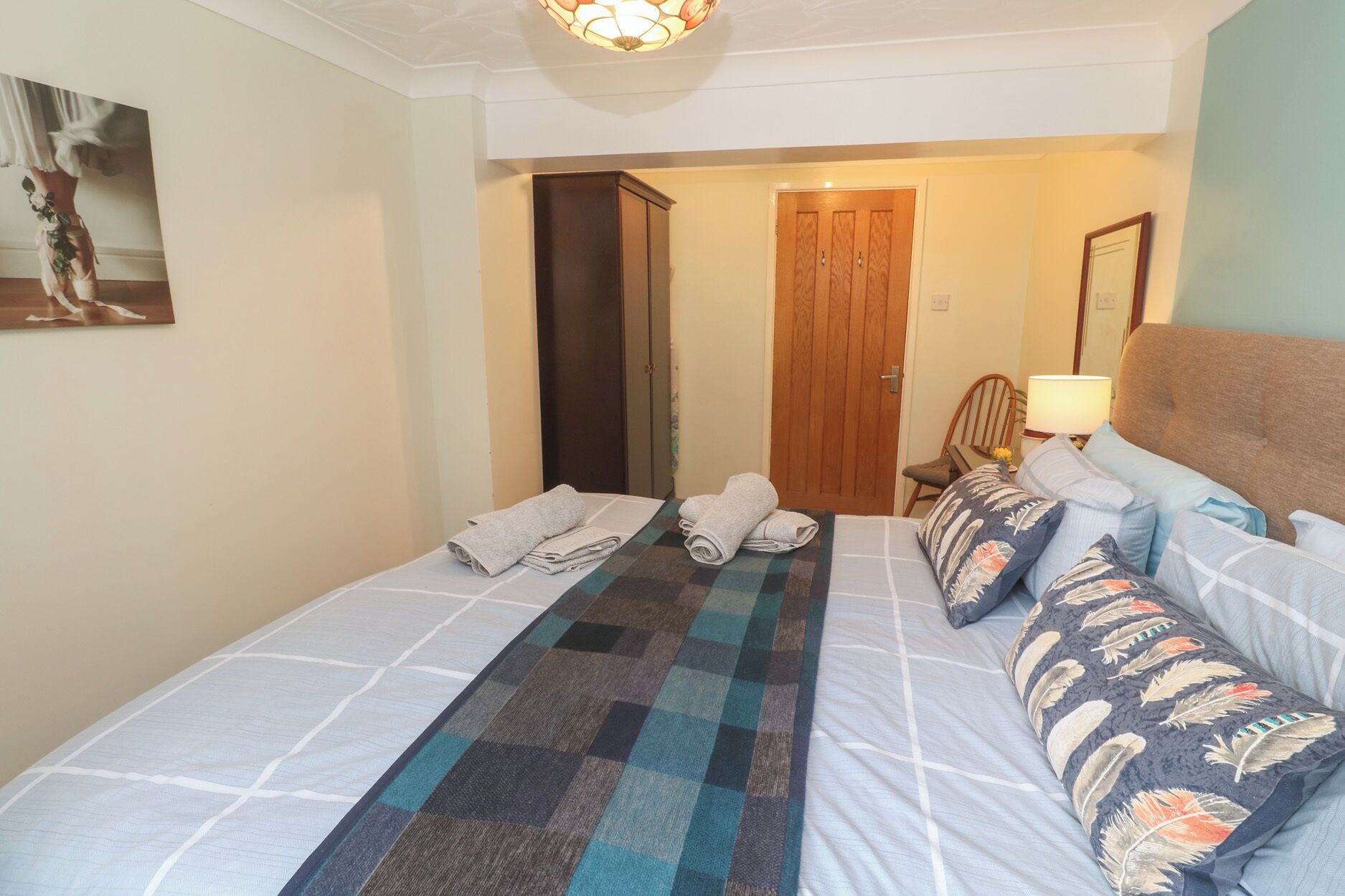 A hotel room with two beds, a checkered runner, a wooden door, a chair, and a lamp.