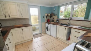 A kitchen with white cabinets, a washing machine, a sink, and a window with a view of greenery.