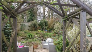 A garden with a wooden pergola, wicker furniture, and potted plants.