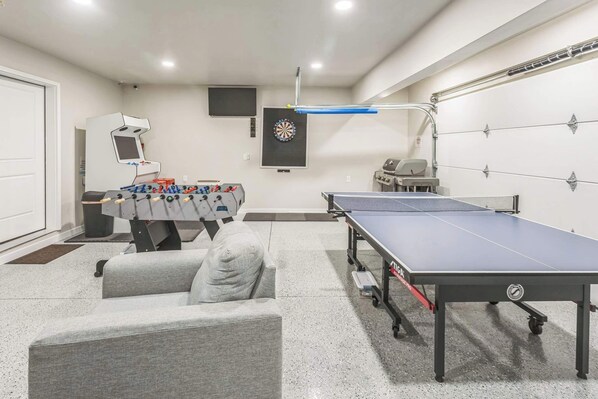 Een kamer met een tafelvoetbaltafel, pingpongtafel, dartbord en een televisie.