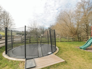 A trampoline with a safety net, surrounded by a wooden fence, and a green slide to the right. - Bell Tent 1 (Bath)