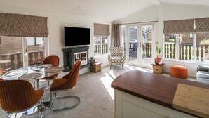 A living room with a fireplace, a television, and a dining area with chairs and a table. - Gressingham View Lodge (Carnforth)