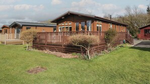 A wooden cabin with a fenced yard, a deck, and a clear sky. - Gressingham View Lodge (Carnforth)