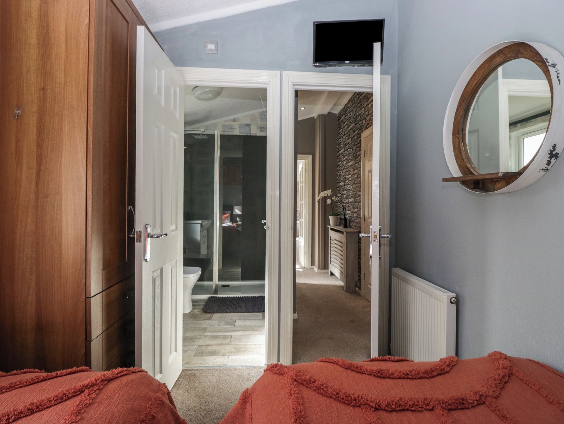 A bedroom with a wooden wardrobe, a television mounted on the wall, and a mirror.