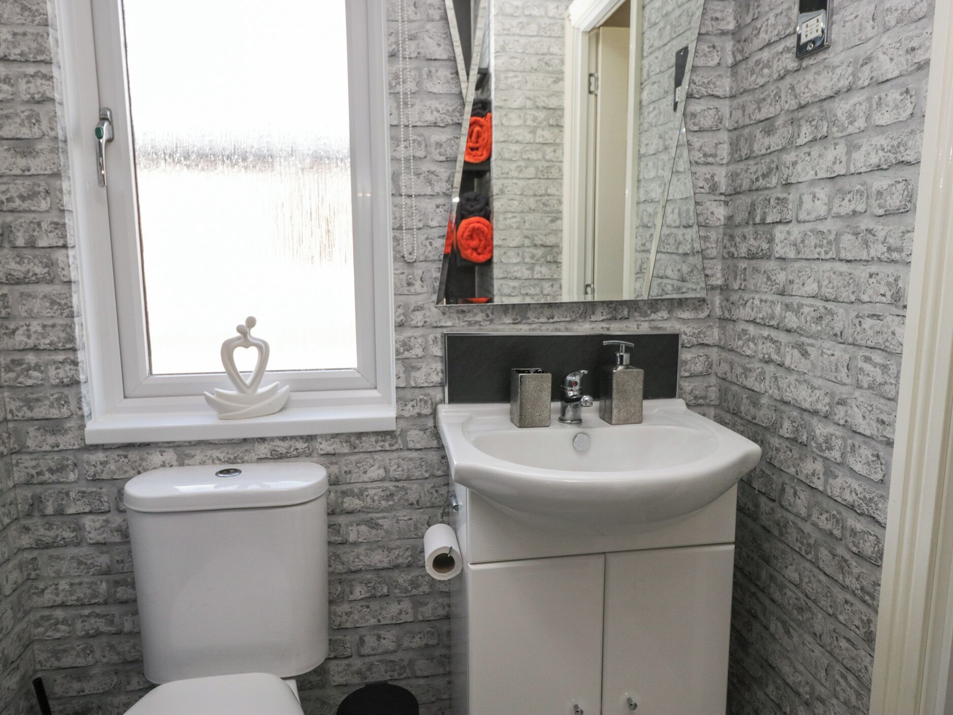 Un bagno con un water bianco, un lavandino con uno specchio sopra e una finestra con cornice bianca.