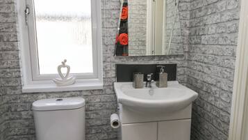 Un bagno con un water bianco, un lavandino con uno specchio sopra e una finestra con cornice bianca.