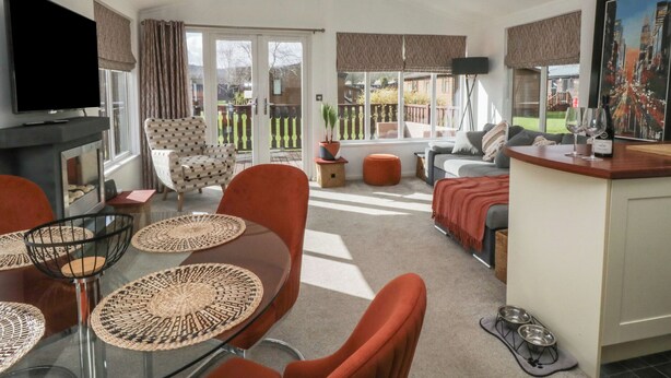 A modern living room with a glass dining table, red chairs, a sofa, and a TV. - Gressingham View Lodge (Carnforth)