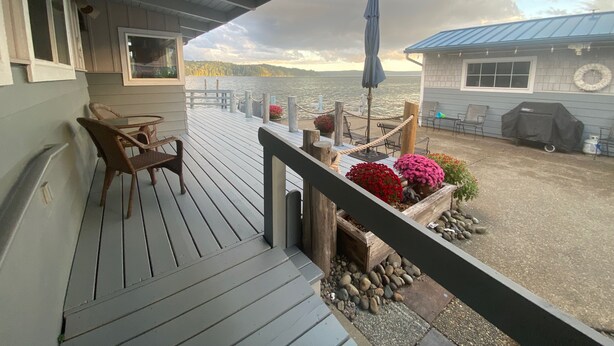 A wooden deck with outdoor seating and a view of a lake. - Water front, private beach, steps from down town Hoodsport with lots of parking. (Hoodsport)