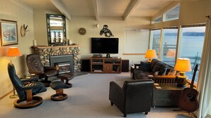 A living room with a stone fireplace, a television, a couch, and a guitar. - Water front, private beach, steps from down town Hoodsport with lots of parking. (Hoodsport)
