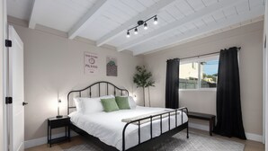 A bedroom with a bed, bedside tables, a window with curtains, a plant, and wall art.