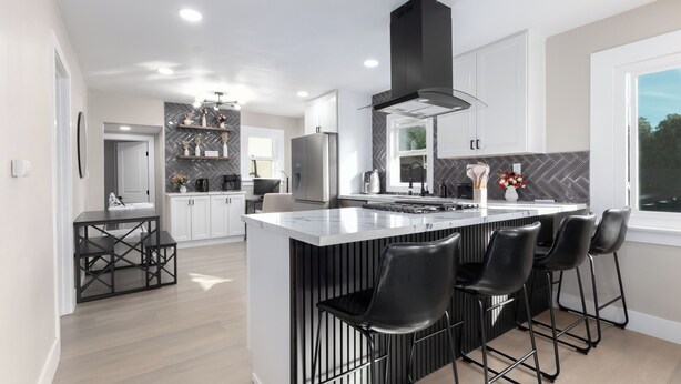 A modern kitchen with a central island, black bar stools, and a black range hood.
