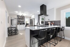 Una cocina moderna con una isla central, taburetes negros y una campana extractora negra.