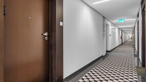 A hotel corridor with a patterned floor, a wooden door, and a white wall with a light switch. - Varsovia Comfort 340 (Warszawa)