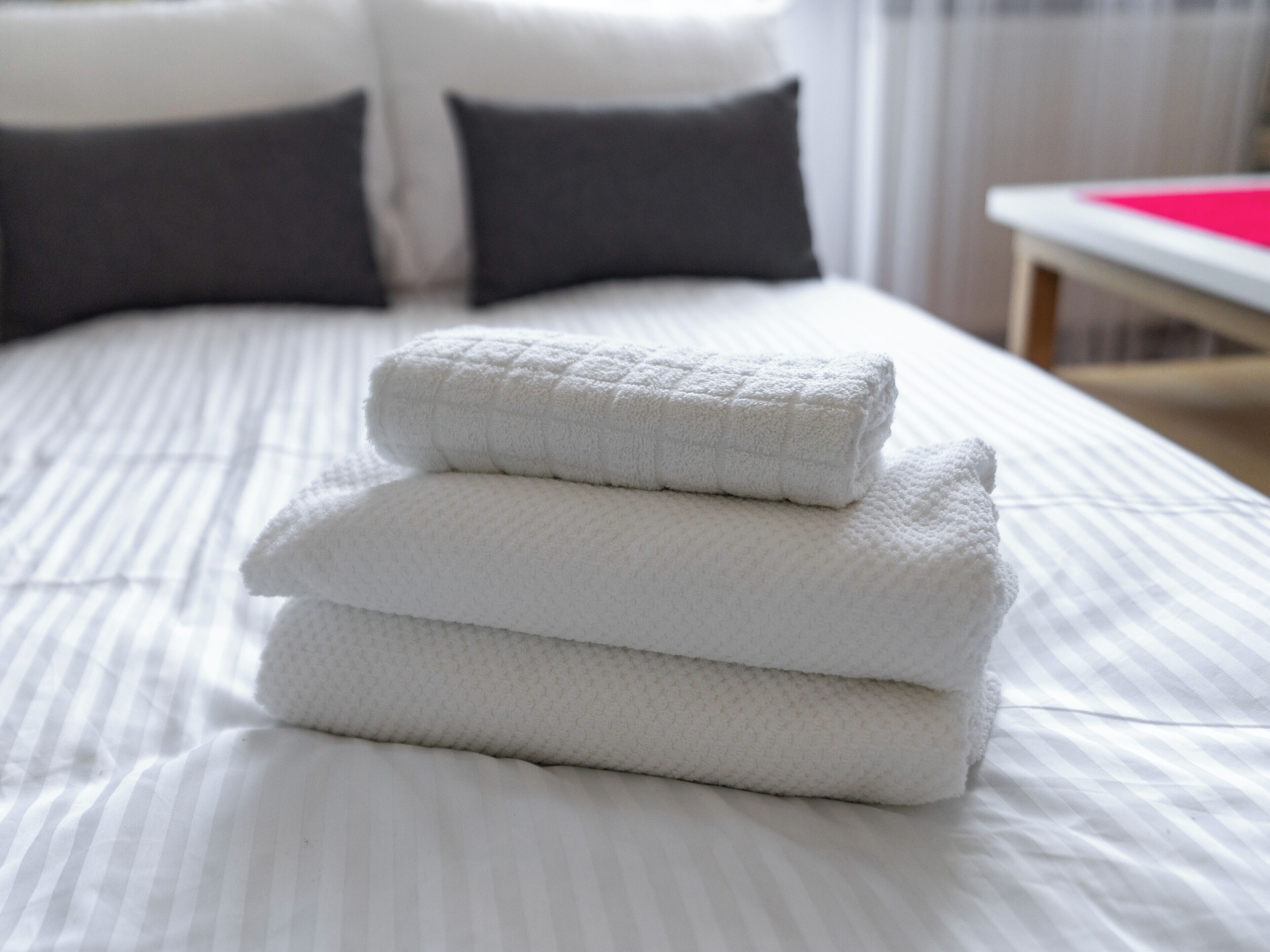 A neatly made bed with white linens and a folded white towel on top.