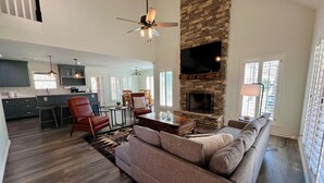A spacious living room with a stone fireplace, a large sofa, and a dining area with a table and chairs. - Spacious Cabin on Little Mo River!! Game Room! Relax & Have Fun! 4 Bed, 4.5 Bath (Murfreesboro)