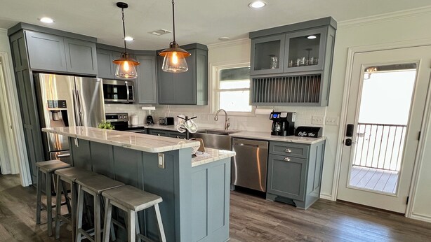 A modern kitchen with grey cabinets, a central island with stools, stainless steel appliances, and pendant lighting. - Spacious Cabin on Little Mo River!! Game Room! Relax & Have Fun! 4 Bed, 4.5 Bath (Murfreesboro)