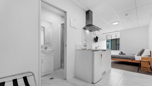 Habitación de hotel moderna y minimalista con kitchenette compacta, cama con estructura de madera y un pequeño espacio para sentarse.