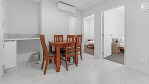 Una habitación moderna y minimalista con una mesa de comedor y sillas, una pequeña kitchenette y una cama en la habitación contigua.