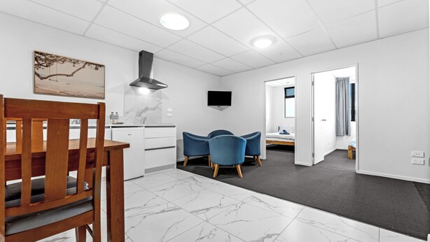 Una habitación de hotel moderna con una mesa de comedor de madera, sillas azules, un televisor de pantalla plana y piso de baldosas de mármol.