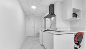 Una cocina moderna con armarios blancos, un microondas integrado y una silla roja.