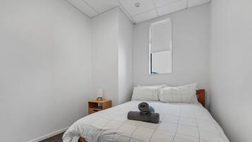 Een slaapkamer met een bed, nachtkastje, raam en een spiegel aan de muur.