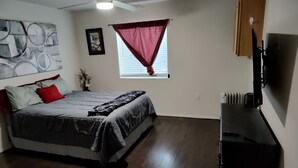 A bedroom with a bed, a ceiling fan, a window with curtains, a radiator, and a TV mounted on the wall. - Charming 1-bedroom cabin in amazing Camp Verde with WiFi, AC, very spacious (Camp Verde)