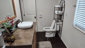 A bathroom with a white sink, toilet, and a metal shelf with towels. - Charming 1-bedroom cabin in amazing Camp Verde with WiFi, AC, very spacious (Camp Verde)