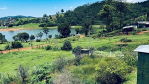A rural landscape with a lake, greenery, and a few buildings in the distance. - Cozy farm in front of the dam, for water sports and fishing. (Serrinha Bragança Paulista)