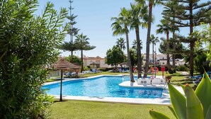 Una piscina rodeada de palmeras y sillas de descanso, con una estructura de techo de paja cerca.