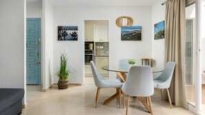 Un comedor moderno con una mesa de vidrio y dos sillas grises, una planta en maceta y una puerta azul.