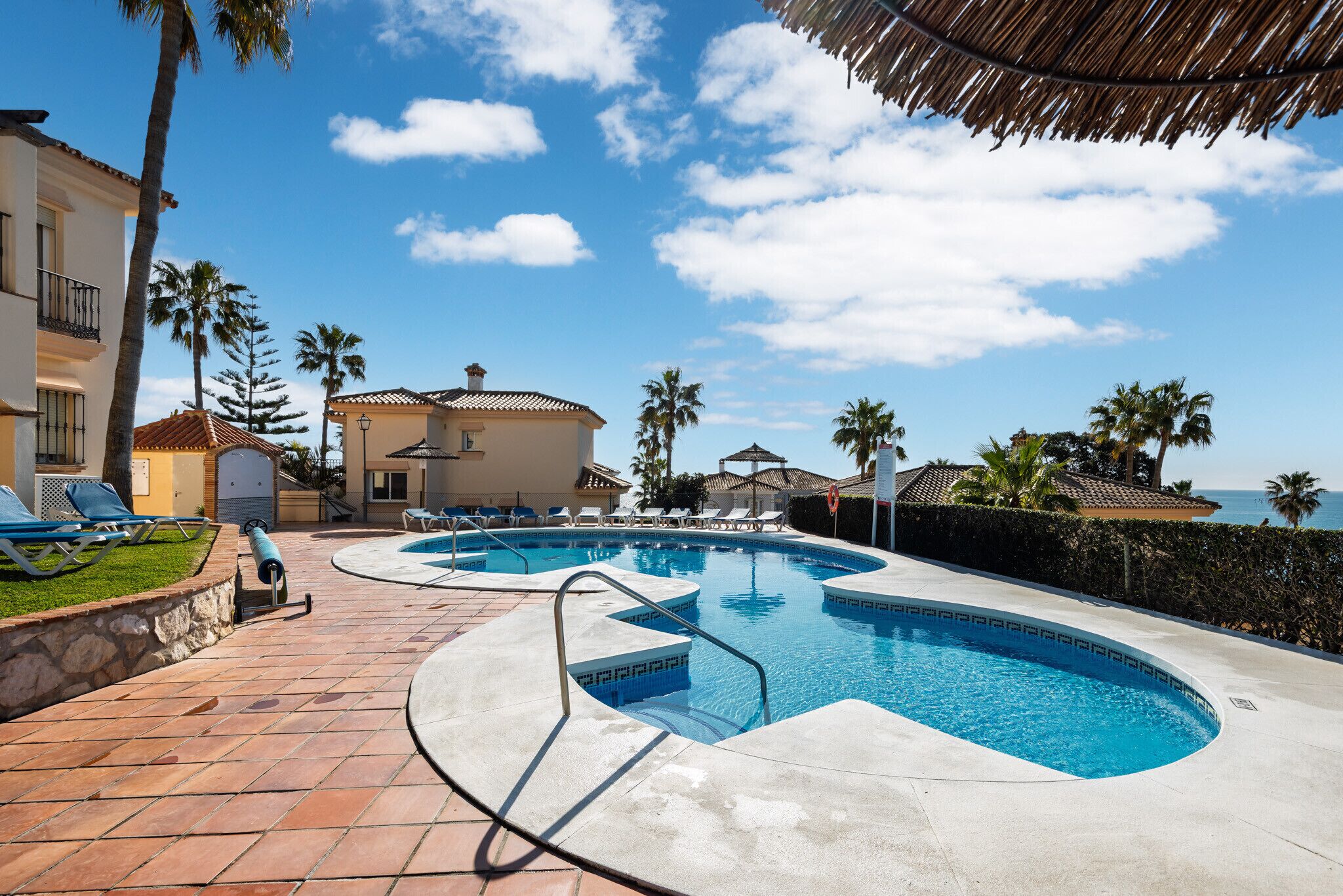 Una piscina de diseño curvo, sillas de descanso y vista al océano.