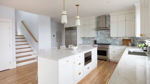A modern kitchen with white cabinetry, a central island, stainless steel appliances, and a marble backsplash. - Luxury Waterfront Home Private Dock, Stunning Views & Sleeps 14 (South Kingstown)