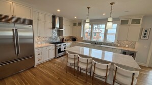 A modern kitchen with a stainless steel refrigerator, a gas stove, and a large island with bar stools. - Luxury Waterfront Home Private Dock, Stunning Views & Sleeps 14 (South Kingstown)
